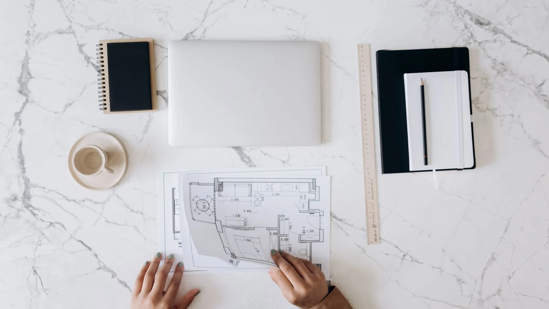 Architectural plans, a laptop, notebooks, and drafting tools arranged on a project worktable